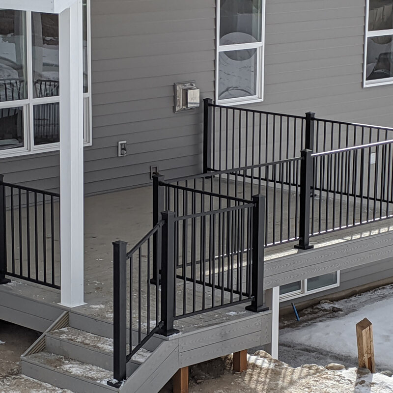 Expand your outdoor living possibilities with this custom grey composite deck by DeckPro LLC. This design provides a safe and stylish transition from your home to your backyard, even in snowy conditions, thanks to durable, low-maintenance composite materials. The contrasting black metal railings and wide steps offer a modern touch while ensuring safe and easy access from the house to the natural terrain below.