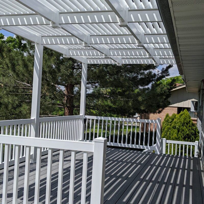 Extend your multi-level outdoor living with this massive multi-zone composite raised deck transformation by DeckPro LLC. Pictured on a beautiful partly cloudy day, this sophisticated structure features expansive gray and brown composite planks paired with sleek black vertical perimeter railings. This sturdy retreat transitions via extensive massive wide staircases with contrasting risers to a stamped concrete lower level and a beautifully landscaped rock garden featuring natural boulder rocks on a gravel bed. Direct access point via multiple existing glass doors and a large massive set of connecting stairs allow for effortless entertaining, while integrated recessed ceiling lighting in the covered upper area ensures evening use. Defining functional zones perfect for both relaxation and large-scale entertaining, this unique tranquilidad sanctuary maximizes spectacular multi-directional natural views.