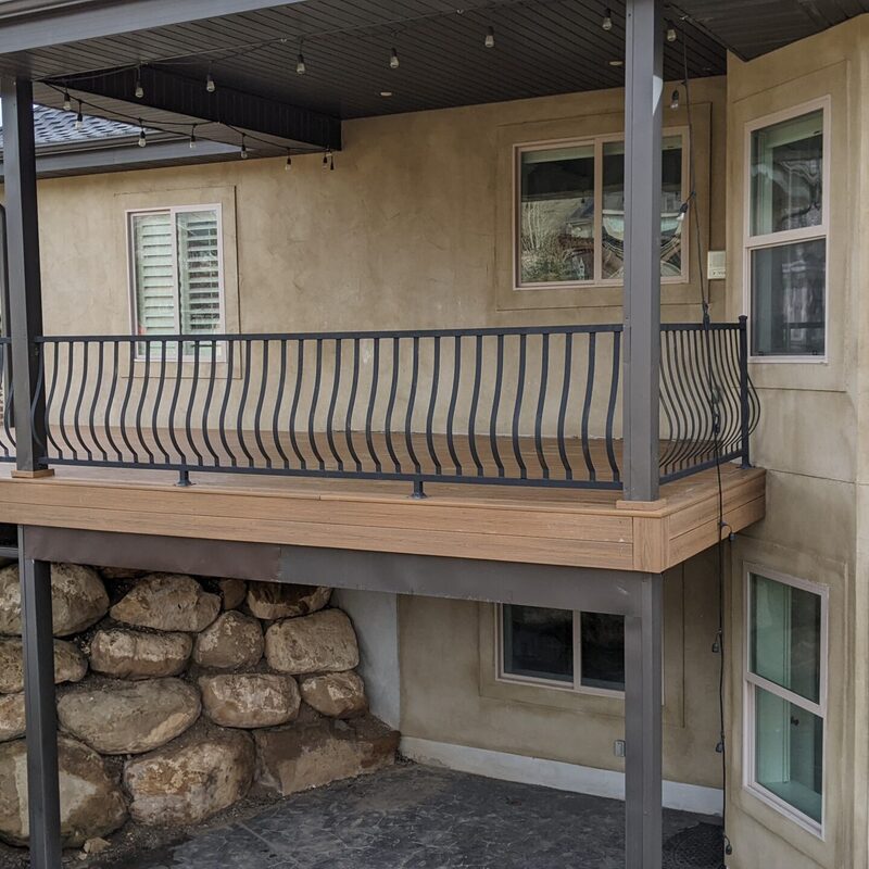 Expand your outdoor living possibilities with this extensive multi-level deck from DeckPro LLC. This custom design features a large upper composite deck area with sophisticated, dark curved metal railings, providing an elevated space for entertaining. Wide, built-in steps lead down, following the natural slope of the landscape to connect with the lower concrete patio, creating a cohesive, functional space that integrates beautifully with the surrounding rock retaining walls.