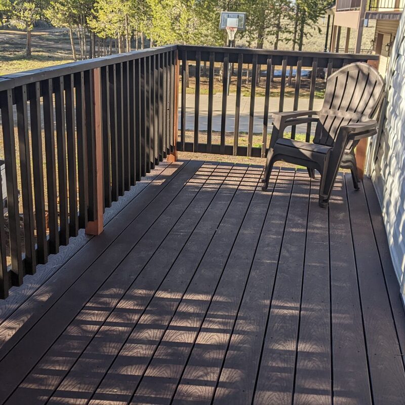 Extend your upper-level living space with this cozy raised composite deck by DeckPro LLC, designed for tranquility and function. We installed low-maintenance composite decking in a warm brown tone and a matching perimeter railing system. Furnished with a comfortable dark Adirondack chair, it's the perfect retreat to take in the serene views of the surrounding pine trees and rustic outdoor setting.