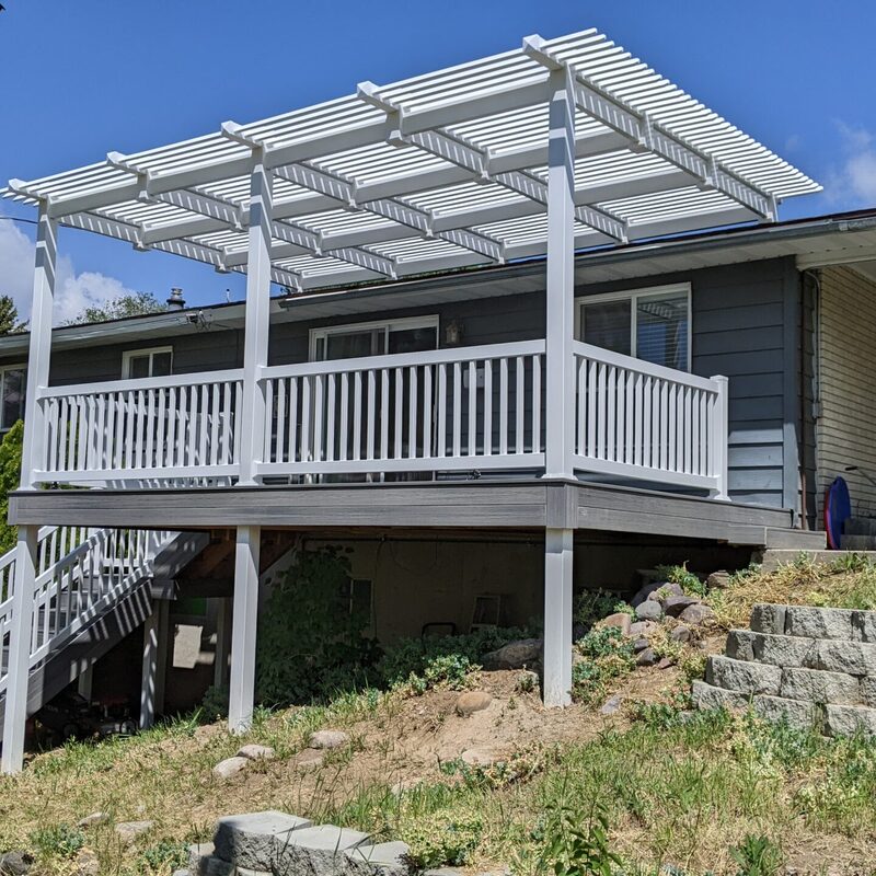 Extend your multi-directional natural views with this rustic custom composite deck by DeckPro LLC. Pictured bordering natural vegetation and a dirt road/trail on a beautiful partly cloudy day, this sturdy retreat transitions smoothly from raised upper levels bordering construction work featuring massive multi-directional natural views of a large lake and mountains. We installed rich brown wood-grain composite decking planks in a unique picture frame board border pattern and paired them with safe and sophisticated rustic timber railings. This functional design includes continuous perimeter railing, defined sun and shade areas bordering construction work, and a custom continuous bench top-rail with metal mesh (hog wire) panel infill. Direct access via multiple conversation areas under covered patio sections with integrated recessed ceiling lighting ensures evening use.
