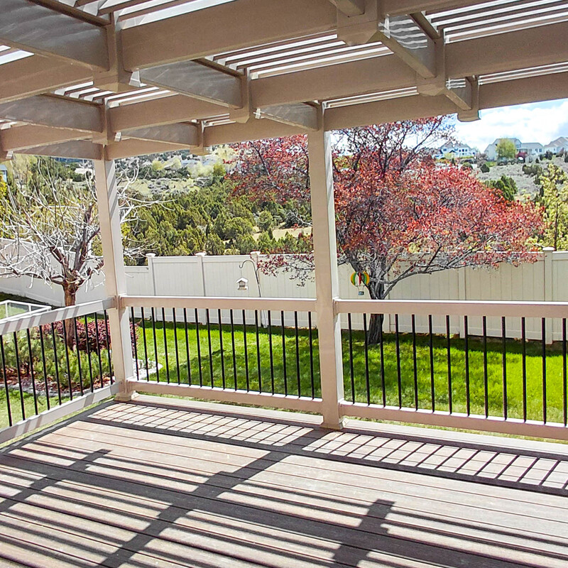 A high-end outdoor living space featuring a low-maintenance tan vinyl pergola for partial shade. The deck is enclosed with modern black metal spindles and matching composite railings, offering a perfect balance of style and durability for Idaho's climate.