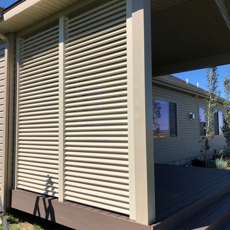 Expand your outdoor living space with this cozy raised deck by DeckPro LLC. We installed high-quality, low-maintenance composite decking in a warm brown tone and paired it with safe and sophisticated dark vertical perimeter railings, creating a sturdy retreat perfect for relaxation. Pictured on a beautiful sunny day with clear skies and distinct shadows cast across the deck boards, this functional build transitions through a massive and inviting set of stairs leading to a stamped concrete patio, creating defined sun and shade areas and optimizing views of the vast backyard. Direct access is available via a sliding glass door.