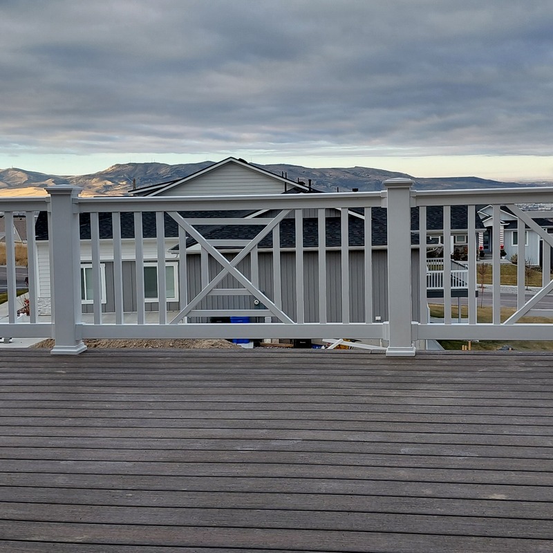 A wide-angle balcony view of a custom vinyl railing installation by DeckPro LLC in Idaho Falls, ID. The project features a unique Chippendale-style "X" pattern integrated into the white vinyl railing system.