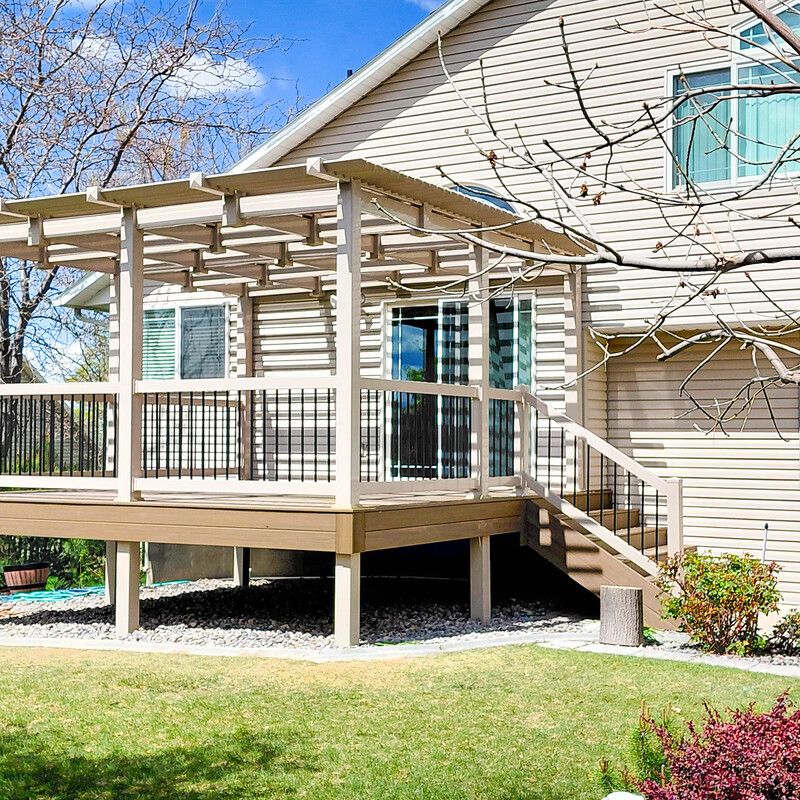A full exterior view of a custom-engineered elevated deck. This project includes a structural pergola for shade, a wide staircase for backyard access, and a clean stone-base finish underneath for maximum drainage and aesthetic appeal. Built by Trex Pro Platinum builders.
