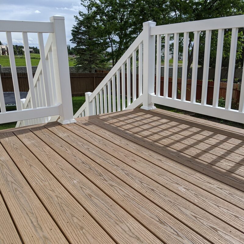 Transform your elevated outdoor space with the signature Apex Custom Elevated Composite Deck by DeckPro LLC. This stunning installation, perfect for homes on sloping lots, features premium high-density wood-grain textured composite decking boards in a rich, multi-tonal brown pattern, providing a durable and sophisticated walking surface. It is safely enclosed by a safe, code-compliant white vertical picket railing system with substantial square posts and decorative caps, ensuring safety without compromising views.