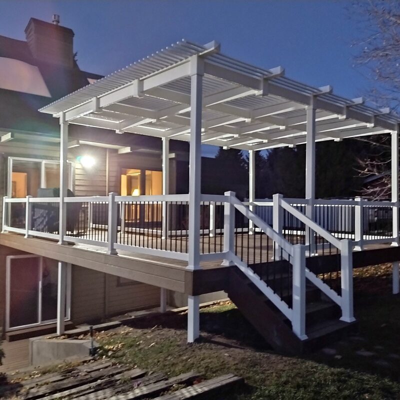 Extend your multi-level outdoor living with this expansive composite deck and patio transformation by DeckPro LLC. We took a multi-story home with rough grading and turned it into a sophisticated, multi-functional sanctuary perfect for large-scale entertaining or tranquil relaxation. Pictured on a beautiful partly cloudy day, this massive structure features multiple defined conversation areas on raised grey composite planks and safe, dark vertical perimeter railings. Direct access points via existing glass doors on multiple levels allow for effortless flow. A large massive wide staircase with contrasting risers leads down to a beautiful stamped concrete lower level transitioning to a restored pool under a prominent covered upper area. Recessed under-deck ceiling lights ensure evening use of this comprehensive build, which also includes complex horizontal slat privacy panels and a meticulously integrated rock garden featuring various bushes and large natural boulder rocks on a gravel bed. This functional retreat maximizes multi-directional natural views for a truly unique tranquillity sanctuary perfect for desert or large properties.