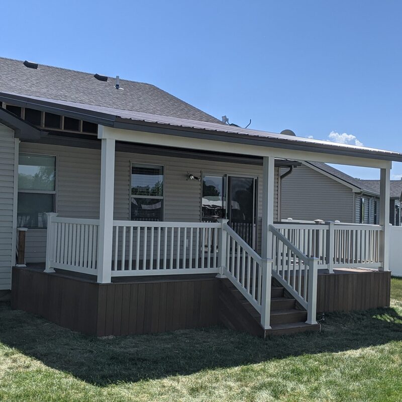 Extend your outdoor living with this dramatic raised composite deck transformation by DeckPro LLC. Pictured on a beautiful partly cloudy day, this sturdy retreat features expansive gray planks with a contrasting picture frame board pattern paired with sleek black vertical perimeter railings. Direct access via existing sliding glass doors ensures effortless flow, while multiple upper-level entry points via comprehensive stairs Transition smoothly from raised upper levels to lower patios bordering natural vegetation and a dirt trail. Integrated recessed ceiling lights under the prominent covered upper area ensure evening use of this functional sanctuary. Multiple conversation areas defined under covered patio sections with hidden enclosed storage with doors transition to lower levels bordering extensive grading work.