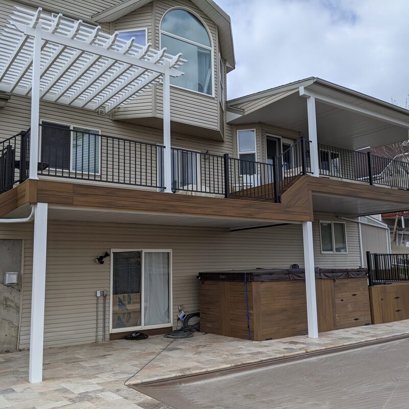 Extend your multi-level outdoor living with this dramatic custom raised deck transformation by DeckPro LLC. Pictured on a beautiful day, this functional retreat seamlessly transitions from a construction phase with framing and raw dirt to a massive and sophisticated tranquility sanctuary. This functional retreat seamlessly connects a raised two-story home featuring stucco siding, horizontal siding, multiple upper-level entry points to a restored pool area and stamped concrete lower patio transition smoothly from raised upper levels to lower patios Bordering a dirt road Transition smooth.