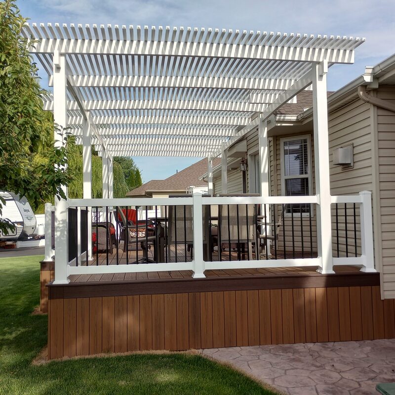 Transform your backyard into a perfect retreat with this custom composite deck and pergola from DeckPro LLC. Enjoy low-maintenance living with durable brown composite decking and a stylish white vinyl pergola that provides refreshing shade. The elegant white railings with black balusters and wide stairs leading to a stamped concrete patio complete this beautiful outdoor living space.