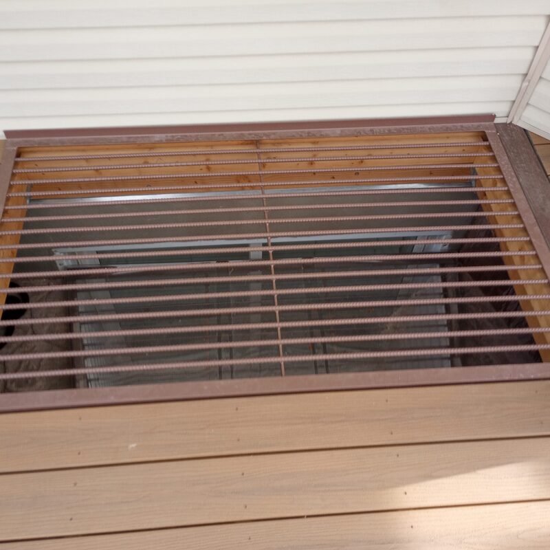 Expand your ground-level living space with this cozy raised deck by DeckPro LLC. Pictured on a beautiful, sunny day with clear skies and distinct shadows cast by the railing, this sturdy retreat uses durable composite decking planks in contrasting brown tones for a classic look. We installed sophisticated dark perimeter railings to ensure safety without obstructing the open views. A massive and inviting set of stairs with matching composite planks leads down to a lower concrete patio, creating defined sun and shade areas perfect for relaxation or entertaining.