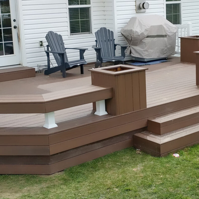 Maximize your backyard entertainment space with this custom ground-level composite deck by DeckPro LLC. Designed for both style and function, it features extensive built-in benches with integrated planter boxes, providing ample seating without cluttering the space. The durable brown composite material ensures a beautiful, low-maintenance finish for years to come.