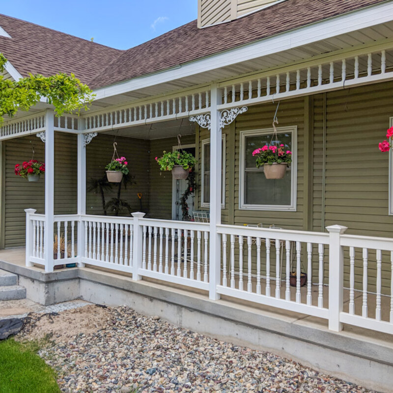 This charming project showcases a complete transformational railing system for a suburban porch. The installation features a durable, clean white vinyl wrap-around railing with elegant turned pickets, providing security and defining the space. The visual centerpiece, however, is the intricate, detailed white spandrel frieze and bracket work installed along the porch roofline, adding immediate traditional character to the green-sided home.