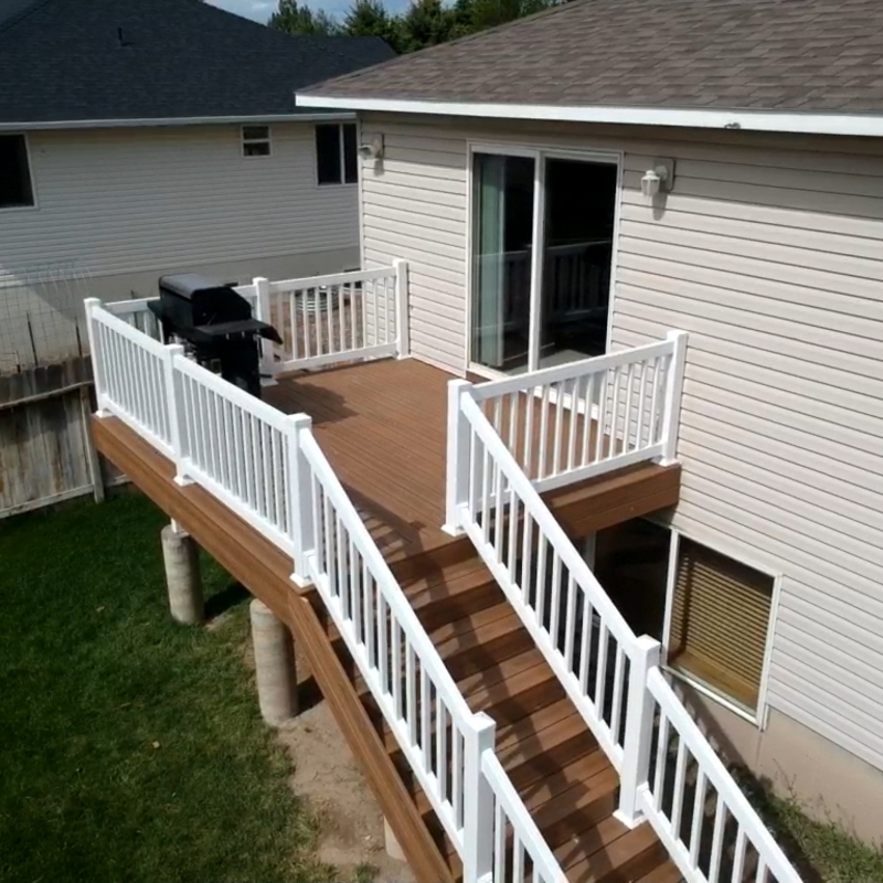 Expand your outdoor living possibilities with this extensive multi-level deck project by DeckPro LLC. We installed high-quality, low-maintenance composite decking in a warm brown tone and paired it with sophisticated black metal perimeter railings that perfectly complement the rustic exterior. Pictured on a beautiful day with distinct railing shadows, the build showcases clean white-framed double doors, connecting your living space to the panoramic forest views. This sturdy and stylish retreat offers the ideal blend of modern durability and classic cabin comfort, perfect for relaxation or entertaining.