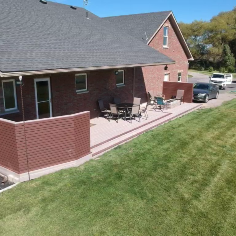 Enhance your outdoor living experience with this custom ground-level deck by DeckPro LLC. Crafted from durable brown composite decking for a low-maintenance finish, this design features extensive built-in perimeter seating and integrated planter boxes, perfect for entertaining. The white post accents provide a crisp contrast, and wide steps offer easy access to the backyard.