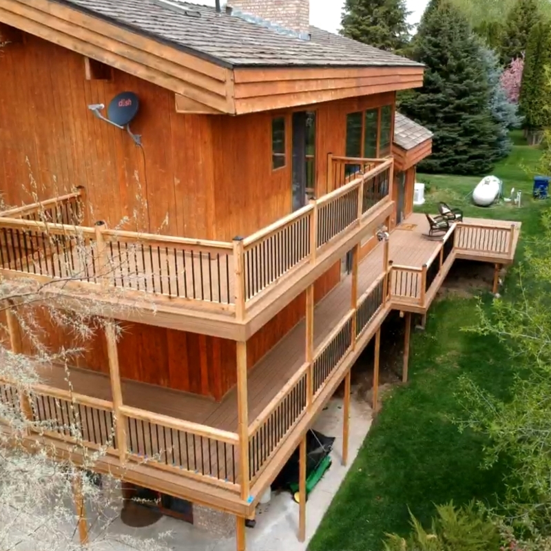 Expand your outdoor living possibilities with this extensive multi-level deck project by DeckPro LLC. Pictured from an aerial perspective on a beautiful day, this massive build features high-quality cedar decking and matching railings with sophisticated black metal balusters. For the ultimate in functional design, we included expansive upper and lower decks connected by a sturdy staircase, all integrated with a lower-level concrete patio. The massive raised structure is designed with extensive space for dining and relaxation, as well as a defined conversation area with metal high-top chairs, creating a truly multi-functional backyard retreat.