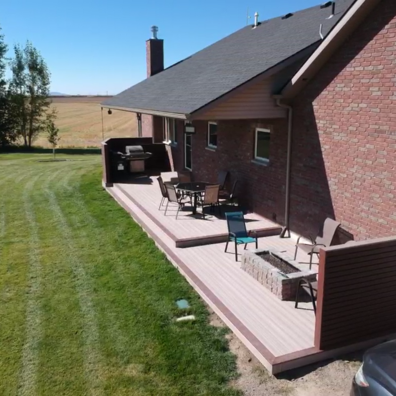 Extend your outdoor living possibilities with this sophisticated composite deck project by DeckPro LLC. We installed durable, low-maintenance composite decking in a warm wood-grain finish, creating a vast and stylish retreat for your backyard. The unique privacy screen system transitions from natural wood components to elegant dark metal balusters, all while including integrated corner privacy panels. For the ultimate in defined functional areas, this build features expansive space for a large conversation set and a complete dining table with patio chairs, perfectly connected by a sturdy staircase to a lower patio. Pictured on a beautiful day with distinct railing shadows, this sturdy design creates a tranquil sanctuary perfect for relaxation and large-scale entertaining.