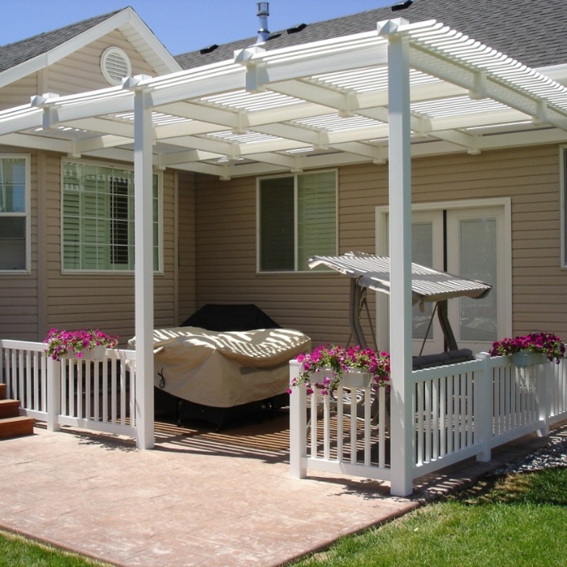 Transform your outdoor living experience with our signature low-maintenance white vinyl attached pergola, featuring a stunning and unique geometric-grid patterned overhead design. This expansive backyard oasis, installed by the experts at DeckPro LLC, seamlessly attaches to the home's rear elevation, creating a massive shaded retreat. The structure is supported by durable posts with elegant caps and includes integrated decorative white vinyl balustrade railings that perfectly define the space.