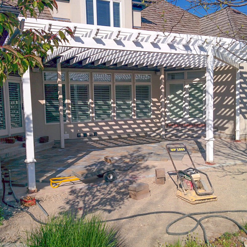 Witness the incredible transformation of a high-end backyard with DeckPro LLC's expert installation services. This image captures the precise craftsmanship and in-progress development of a grand, attached louvered pergola system covering a newly laid custom paver patio. DeckPro LLC is seamlessly integrating a large white multi-bay pergola structure, supported by elegant posts, with the client's luxurious home, defined by its expansive windows.
