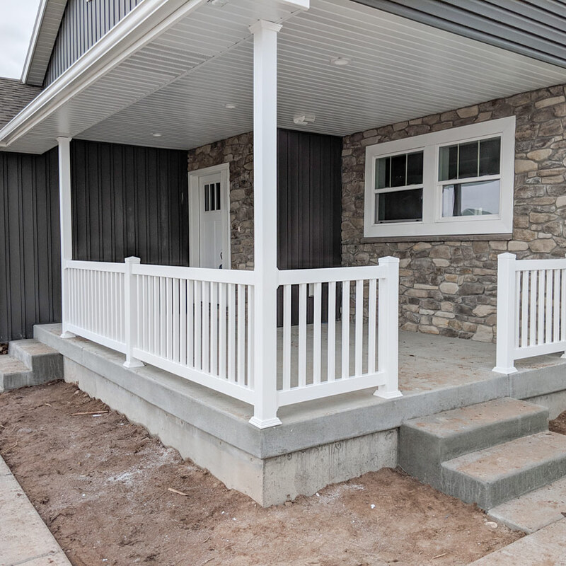 A detailed view of a newly completed front porch project in Sandy, featuring clean, durable white vinyl railings. This L-shaped system with traditional square pickets defines the concrete porch area, providing a safe and stylish enclosure.
